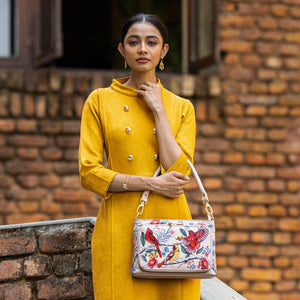 A woman wearing a mustard yellow dress and holding a floral-patterned Anuschka Large RFID Organizer - 684 stands in front of a brick wall.