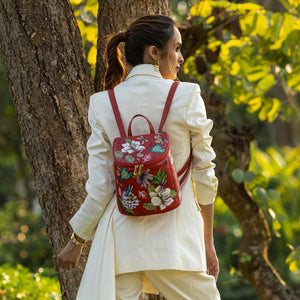 Woman with a Anuschka genuine leather floral Bucket Backpack - 685 featuring adjustable straps, standing by a tree.