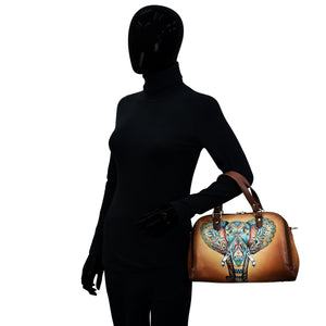 A mannequin dressed in a black turtleneck and gloves holding an Anuschka Wide Organizer Satchel - 695 decorated with hand-painted artwork.
