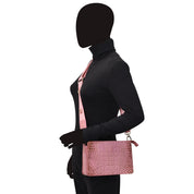 A person with a blacked-out face wearing a black turtleneck and pink vest, holding an organized Anuschka Triple Compartment Crossbody - 696 with compartments, against a white background.