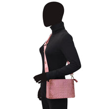 Load image into Gallery viewer, A person with a blacked-out face wearing a black turtleneck and pink vest, holding an organized Anuschka Triple Compartment Crossbody - 696 with compartments, against a white background.
