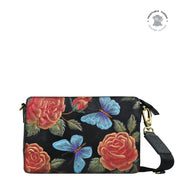 The Anuschka Triple Compartment Crossbody - 696 is a black genuine leather clutch adorned with rose and butterfly designs, complete with a detachable adjustable strap, triple compartment functionality, and elegant gold hardware.