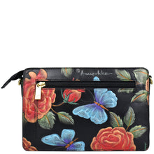 Load image into Gallery viewer, The Anuschka Triple Compartment Crossbody - 696 is a black, genuine leather bag adorned with floral and butterfly art. It includes a front zipper pocket with a gold zipper pull and has an adjustable strap for added convenience. The bag offers triple compartments for organized storage.
