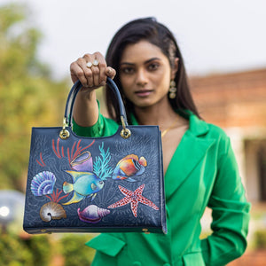 A woman in a green blazer holding a chic Anuschka Medium Satchel - 697 with a colorful marine life design.