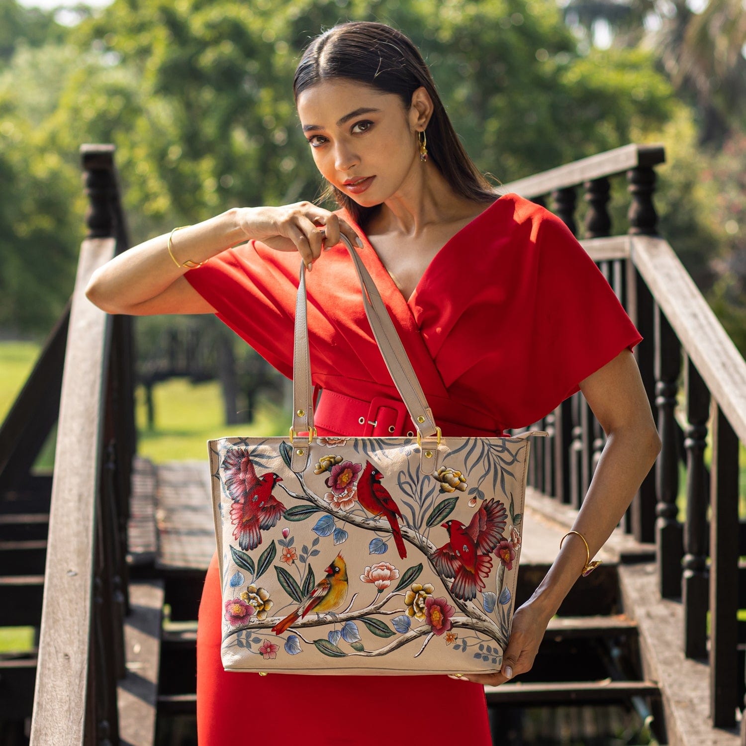 Woman posing with an Anuschka Large Zip Top Tote - 698 on a bridge in a park.