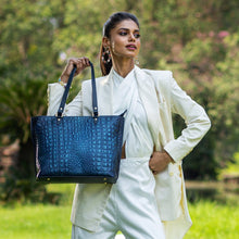 Load image into Gallery viewer, A confident woman modelling a white suit and holding a blue textured Anuschka Large Zip Top Tote - 698 bag outdoors.
