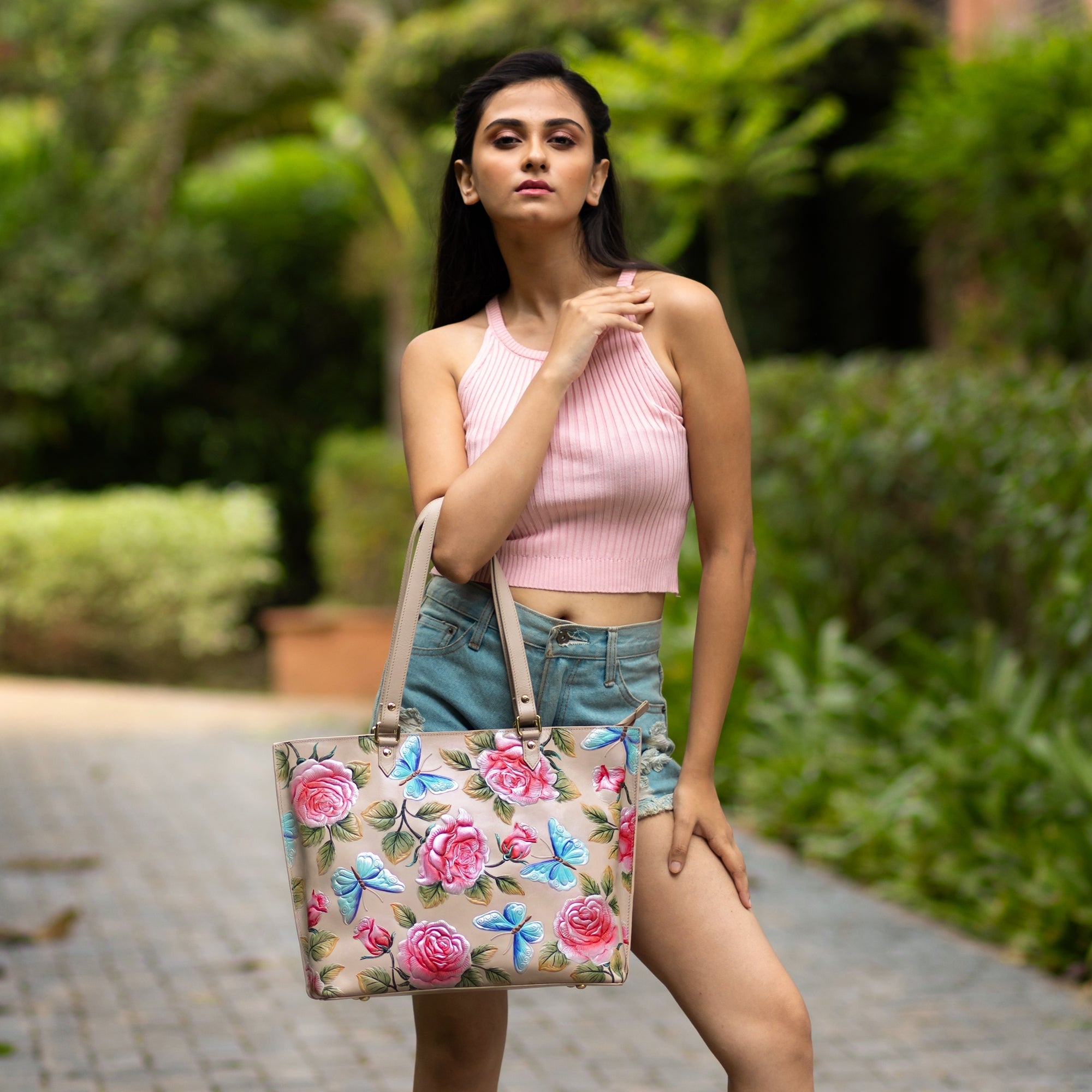 A woman posing outdoors with a Anuschka Large Zip Top Tote - 698, hand-painted with florals.