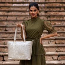 Load image into Gallery viewer, Woman posing with a Anuschka white embossed leather tote, wearing a green dress against a brick stair backdrop.
