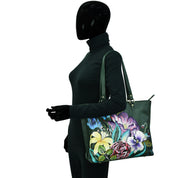 A mannequin dressed in black displays a green, genuine leather Anuschka Large Zip Top Tote - 698 adorned with colorful, hand-painted artwork.