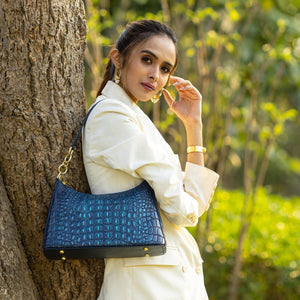 Woman in a white outfit posing with an Anuschka Hobo With Chain Strap - 707 genuine leather blue handbag near a tree.