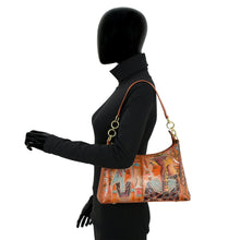 Load image into Gallery viewer, A mannequin dressed in black showcases a sophisticated Anuschka Zip-Top Shoulder Hobo - 707, featuring colorful, Egyptian-inspired artwork. The bag, carried on the shoulder with a chain detail shoulder strap, offers both style and practicality.
