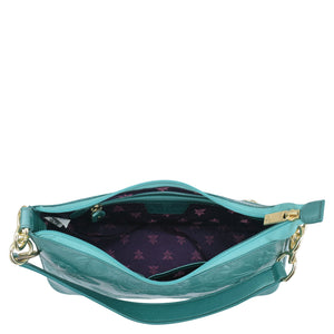 Open Anuschka turquoise genuine leather exterior handbag with an empty interior and floral pattern lining.