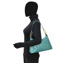 Load image into Gallery viewer, Mannequin displaying a turquoise leather Anuschka hobo bag with floral embossing and a chain detail shoulder strap.
