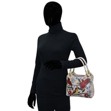 Load image into Gallery viewer, Mannequin dressed in black wearing gloves and carrying an Anuschka leather, floral print Satchel With Crossbody Strap - 708 handbag.
