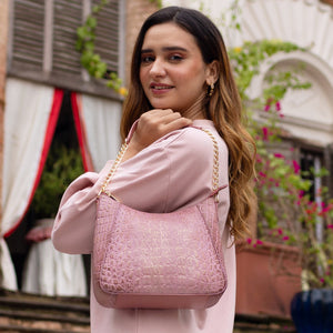 A woman in a pink outfit showcasing an Anuschka Zip-Top Shoulder Hobo - 709 with chain link detail outdoors.