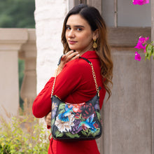 Load image into Gallery viewer, A woman in a red outfit with an Anuschka Zip-Top Shoulder Hobo - 709 over her shoulder, looking over her shoulder at the camera.
