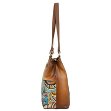 Load image into Gallery viewer, Side view of the Anuschka Medium Everyday Tote - 710, a brown genuine leather tote bag adorned with intricate, colorful patterns including eyes and shapes on one side. The bag features a sturdy strap, multiple pockets, and brass hardware attachments.
