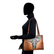 Silhouette of a person dressed in black holding the Anuschka Medium Everyday Tote - 710, featuring an intricate and colorful elephant design on genuine leather.