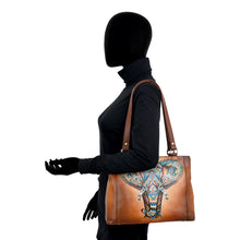 Load image into Gallery viewer, Silhouette of a person dressed in black holding the Anuschka Medium Everyday Tote - 710, featuring an intricate and colorful elephant design on genuine leather.
