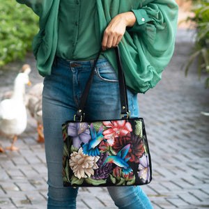 Woman holding a hand-painted, floral-print Medium Everyday Tote - 710 by Anuschka with a duck in the background.