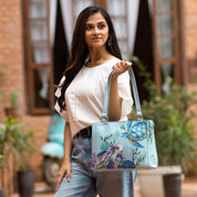 Woman holding a Anuschka Medium Everyday Tote - 710 with hand-painted marine life, standing in a courtyard.