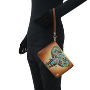 A person in black clothing carries the Anuschka 4 in 1 Organizer Crossbody - 711, a genuine leather brown wristlet adorned with a colorful, detailed elephant design and featuring a removable crossbody strap.