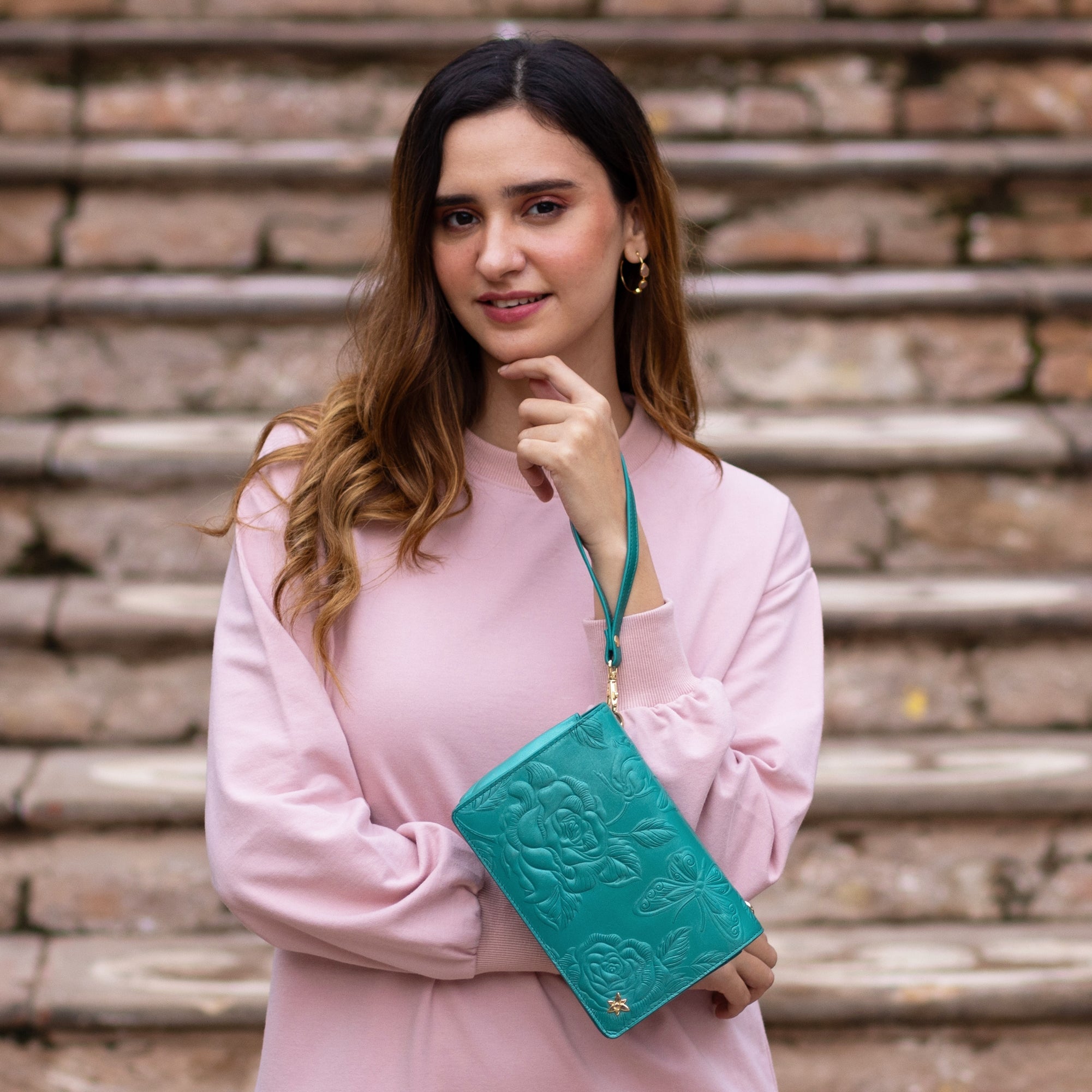 Woman holding a Anuschka 4 in 1 Organizer Crossbody - 711 with a crossbody strap standing in front of brick stairs.