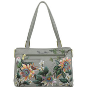 A spacious tote with two straps and a zippered front pocket, this gray Expandable Shopper Tote - 712 features a colorful hand-painted floral design on genuine leather. The brand name "Anuschka" is prominently displayed on the front.