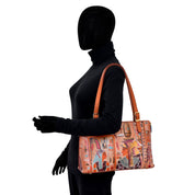 A mannequin dressed in black displays the spacious Anuschka Expandable Shopper Tote - 712, featuring Egyptian-themed artwork with hand-painted hieroglyphics and ancient Egyptian figures, held by its straps over the mannequin's shoulder.