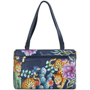 The Anuschka Expandable Shopper Tote - 712 is a navy blue handbag featuring two shoulder straps and adorned with a vibrant design of leopards, flowers, and a butterfly. This genuine leather tote masterfully combines elegance with durability.