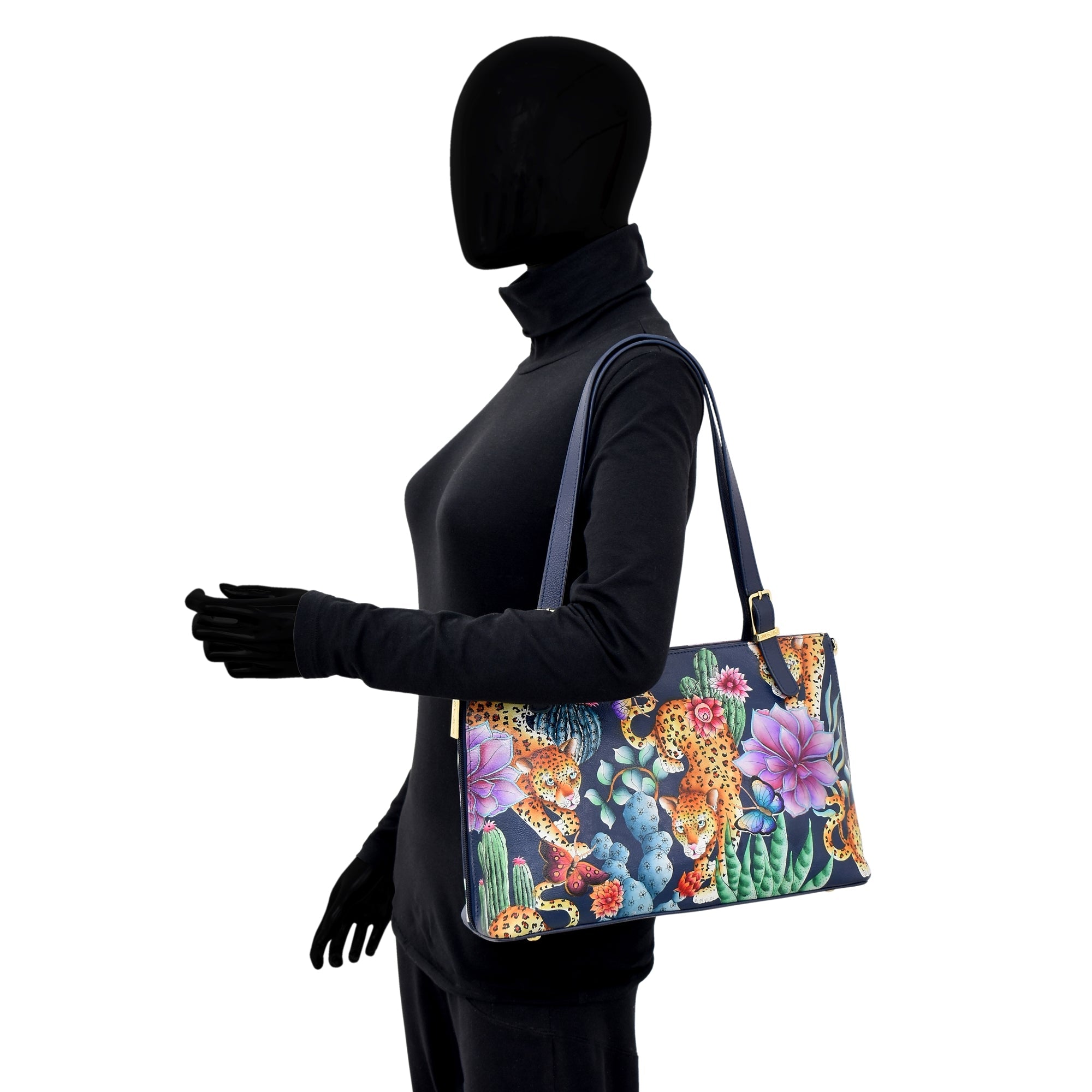 A black mannequin dressed in a sleek black outfit holds an Anuschka Expandable Shopper Tote - 712 with floral and nature-inspired prints over its shoulder, complete with an adjustable handle for convenience.