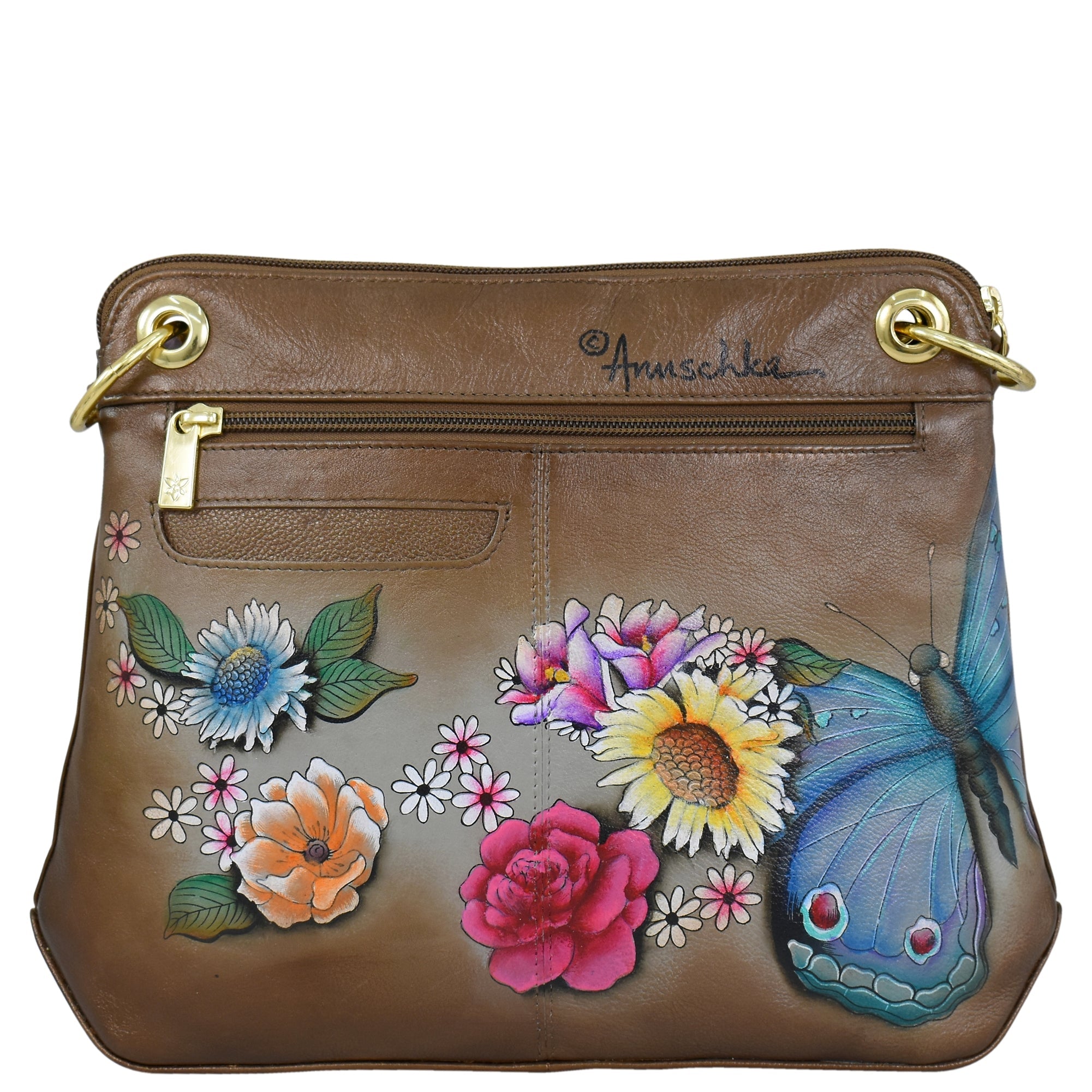 Anuschka’s Crossbody Sling Bag - 713 is a brown leather handbag adorned with colorful hand-painted artwork of flowers and a blue butterfly, featuring a zippered pocket, gold-tone hardware, and an adjustable crossbody strap.