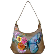 The Anuschka Slim Shoulder Hobo - 714 is a genuine leather handbag adorned with a floral and butterfly design in vibrant hues of pink, yellow, and blue. This everyday bag features a single shoulder strap.