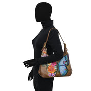 Silhouette of a person wearing a black turtleneck and holding an Anuschka Slim Shoulder Hobo - 714, a genuine leather bag adorned with colorful floral and butterfly designs.