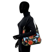 A mannequin in a black turtleneck showcases a modern Anuschka Slim Shoulder Hobo - 714 with a floral and butterfly pattern on its right shoulder, featuring an adjustable strap for versatile wear.