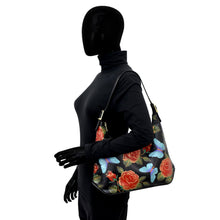 Load image into Gallery viewer, A mannequin in a black turtleneck showcases a modern Anuschka Slim Shoulder Hobo - 714 with a floral and butterfly pattern on its right shoulder, featuring an adjustable strap for versatile wear.
