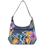 Anuschka's Slim Shoulder Hobo - 714 is a blue handbag crafted from genuine leather, adorned with a vibrant painted design showcasing leopards, flowers, and cacti. This modern hobo style features a single strap and gold zipper details, making it the perfect everyday bag.