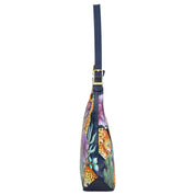 Side view of the Slim Shoulder Hobo - 714, a blue genuine leather handbag by Anuschka, adorned with a jungle-themed print featuring leopards and foliage. This modern Hobo bag showcases gold hardware and a blue strap, making it an ideal choice for everyday use.