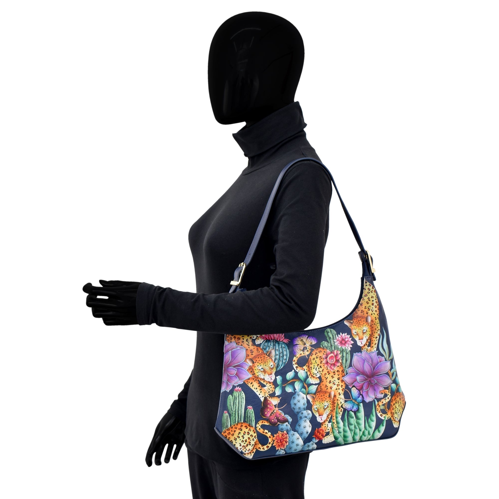 Mannequin in black turtleneck and pants displaying the Anuschka Slim Shoulder Hobo - 714, a colorful shoulder bag with a vibrant floral and tiger design, crafted from genuine leather.