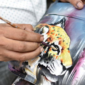Artist painting a colorful design on an Anuschka Slim Crossbody With Front Zip - 452 in dark forest green.