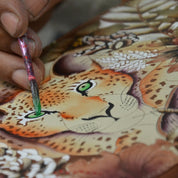 An artist's hand painting details on a Anuschka Classic Hobo With Studded Side Pockets - 433.