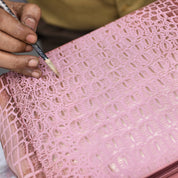 A person meticulously hand-paints a pattern on a pink, textured genuine leather Three Fold Wallet - 1150 by Anuschka.