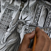 A person paints a hand-painted, silver-colored illustration of the Statue of Liberty and surrounding urban structures on an Anuschka Crossbody Sling Bag - 713.