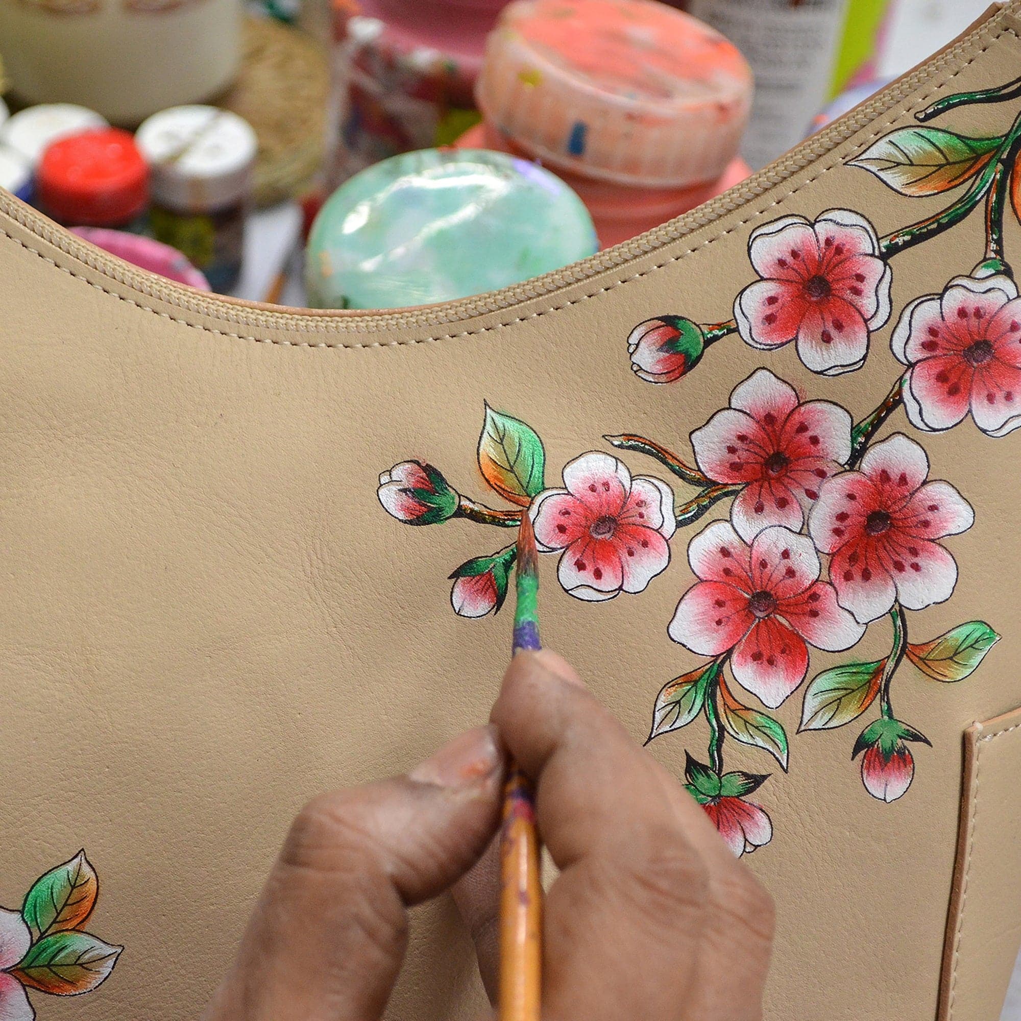 Hand painting floral designs on an Anuschka Classic Hobo With Side Pockets - 382 genuine leather beige handbag.