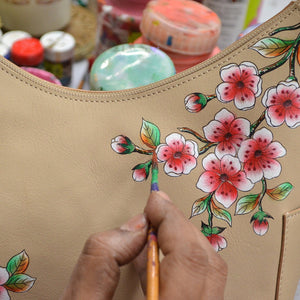 Hand painting floral designs on an Anuschka Classic Hobo With Side Pockets - 382 genuine leather beige handbag.