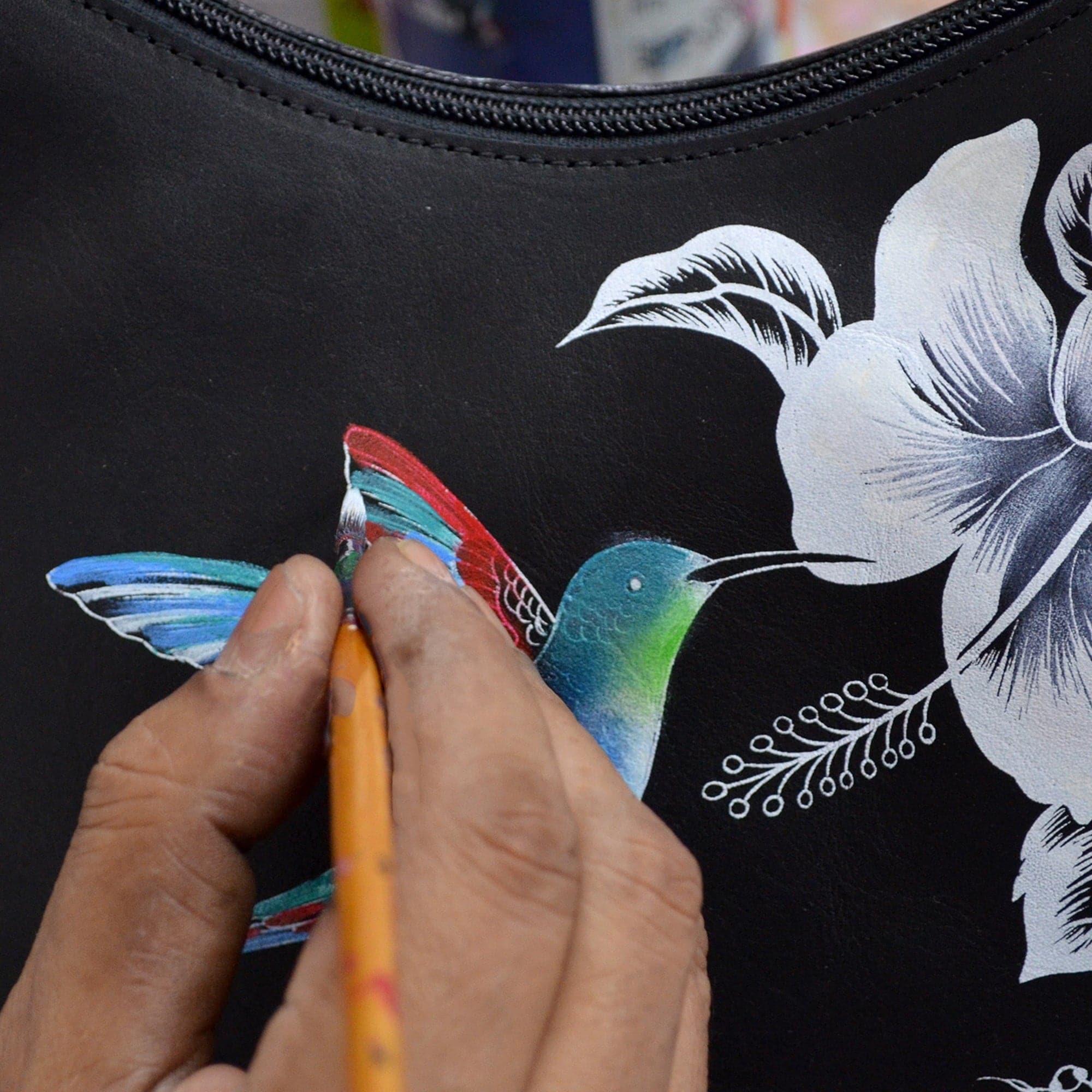 Hand painting a hummingbird design on an Anuschka Classic Hobo With Side Pockets - 382 genuine leather black handbag.