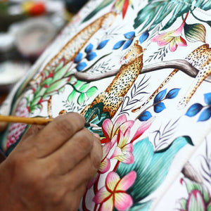 An artist's hand painting intricate floral and leopard designs on genuine leather for a chic Anuschka Classic Hobo With Side Pockets - 382 handbag.