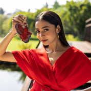 Woman in a red dress holding a hand-painted, bird-shaped Anuschka Painted Leather Bag Charm K0038 outdoors.