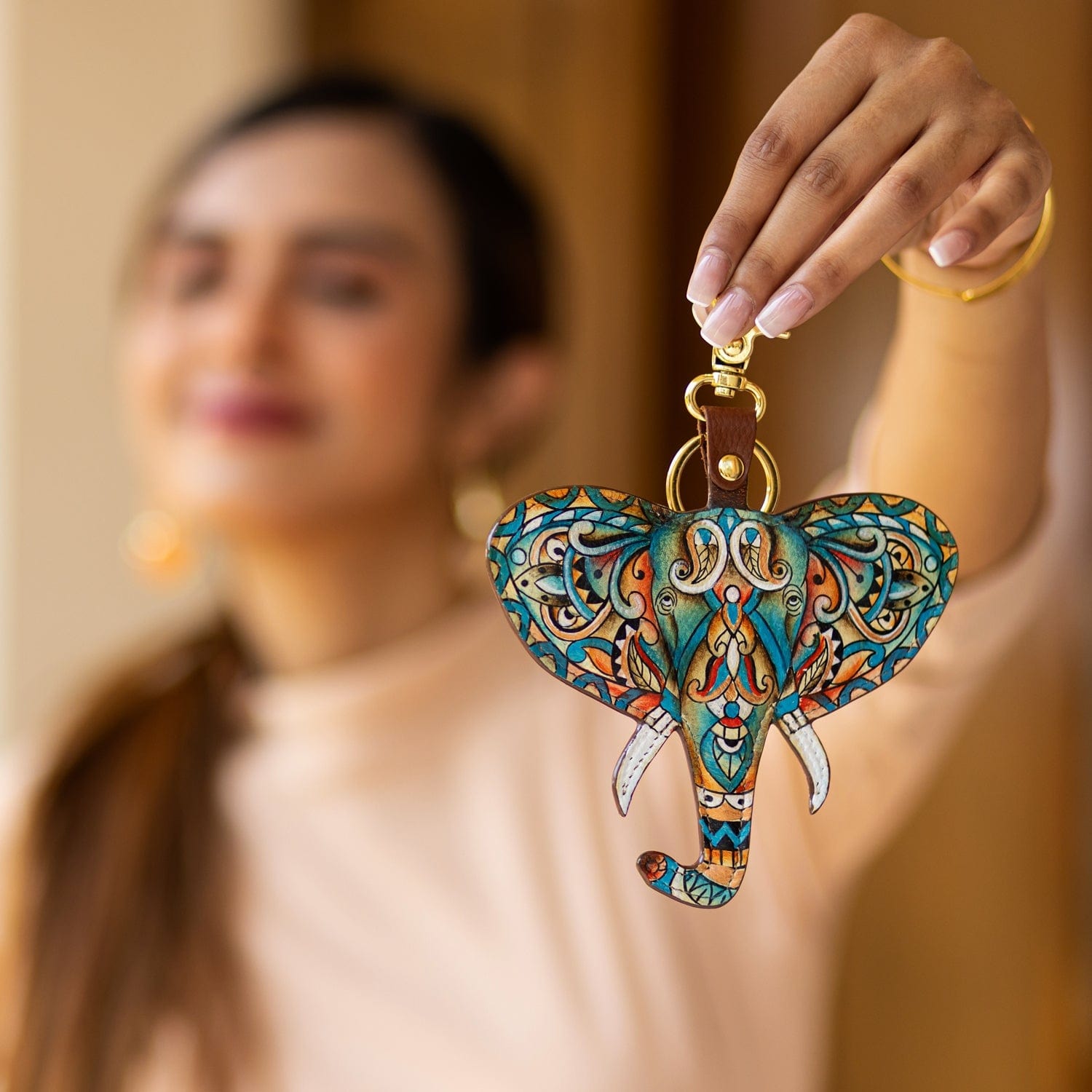 A person holding a Anuschka Painted Leather Bag Charm K0039 - Keycharms in focus, with their smiling face blurred in the background.