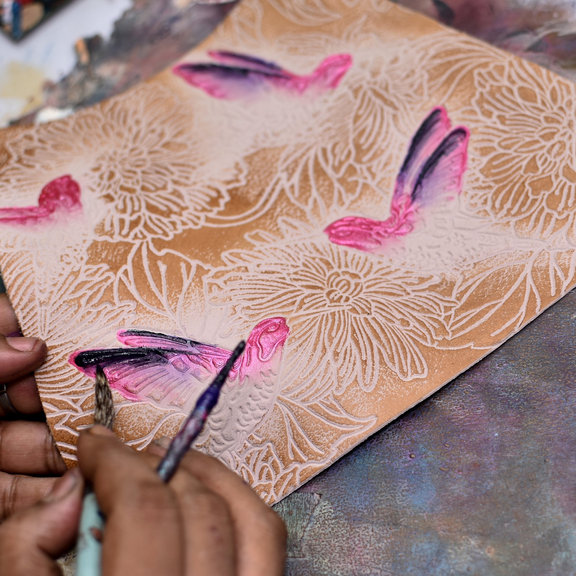 An artist's hands painting colorful bird motifs on an Anuschka Zip-Top Shoulder Hobo - 709.